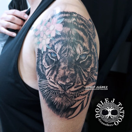 Tatuaje de tigre de ojos azules realista con sombras y texturas detalladas en el antebrazo, diseño personalizado por Doble J Tattoo.