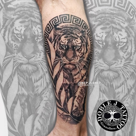Tatuaje de tigre y laurel realista con sombras y texturas detalladas en el antebrazo, diseño personalizado por Doble J Tattoo.
