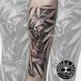 Tatuaje de tigre entre hojas realista con sombras y texturas detalladas en el antebrazo, diseño personalizado por Doble J Tattoo.