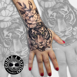 Tatuaje de tigre y flores realista con sombras y texturas detalladas en la mano, diseño personalizado por Doble J Tattoo.